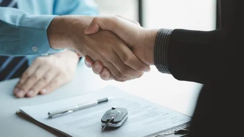 Zwei Personen geben sich über einem Vertrag mit einem Autoschlüssel die Hand