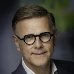 Porträt von Michel van Roon mit runder dunkler Brille, in dunkelblauem Sakko und weißem Hemd ohne Krawatte