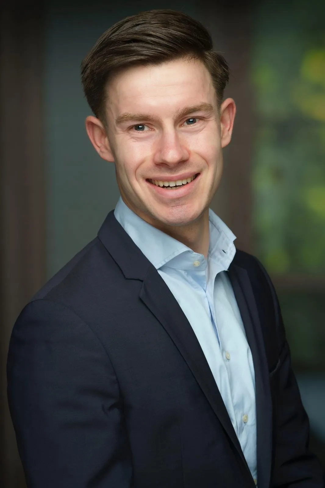 Portrait of Tom Hessing, smiling, in a dark jacket and light blue shirt